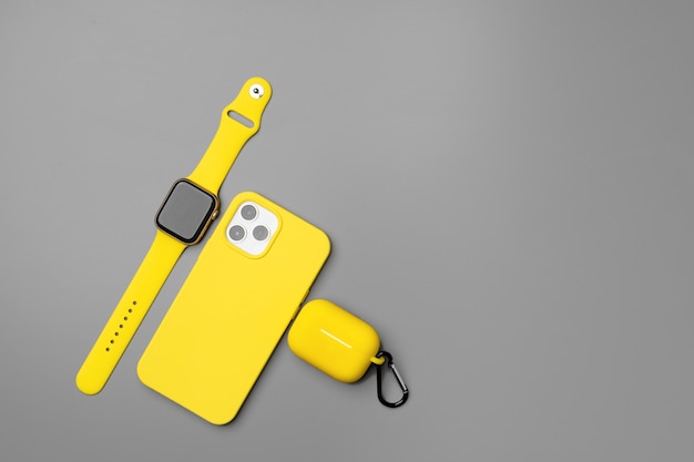 Yellow smartphone, smartwatch and earphones on gray background