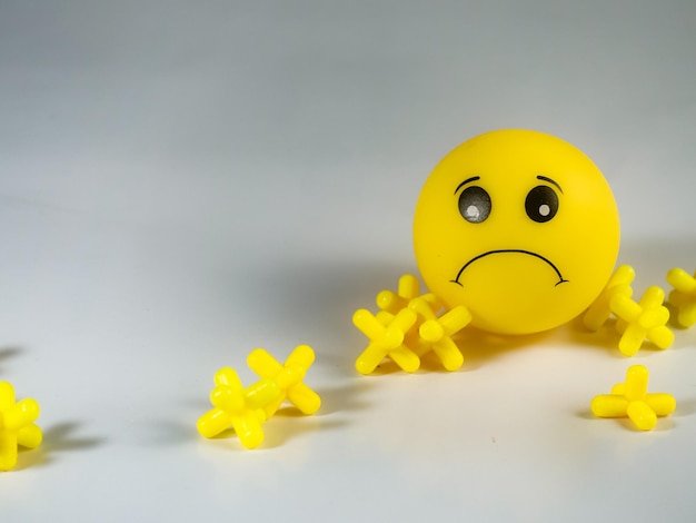 A yellow smiley face is laying on the floor with one of his arms folded and the other has a sad face.