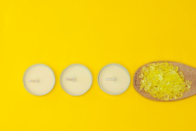 Yellow spa sea salt on a wooden spoon and aroma candles on yellow background