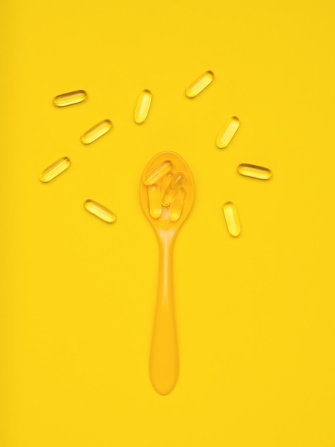 Yellow spoon and fish oil capsules on a yellow background Biologically active additive