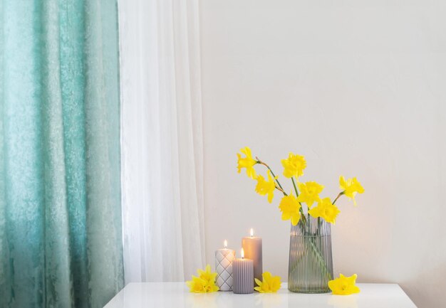 yellow spring daffodils in glass vase with burning candles on white background