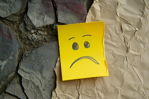 Yellow Sticky Note with Sad Face on Crumpled Paper Background