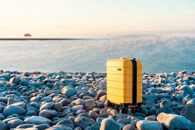 Yellow Suitcase with an orange scarf on the seaside against the sea Travel concept