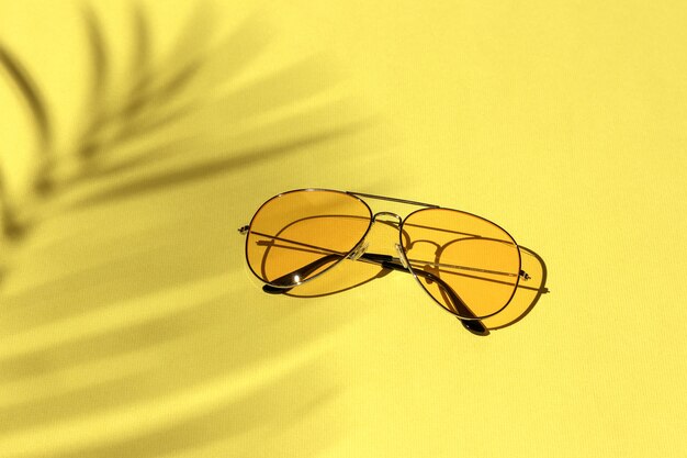 Yellow sunglasses on a pastel background under a palm tree shadow. leisure, travel and entertainment concept with copy space