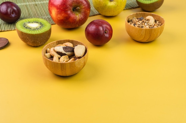 Yellow table with fresh fruits such as apple kiwi plum pear chestnuts and granola