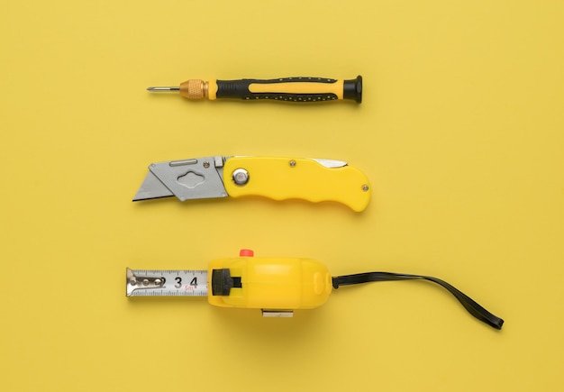 Yellow tape measure knife and screwdriver on a yellow background Tools for creativity Flat lay