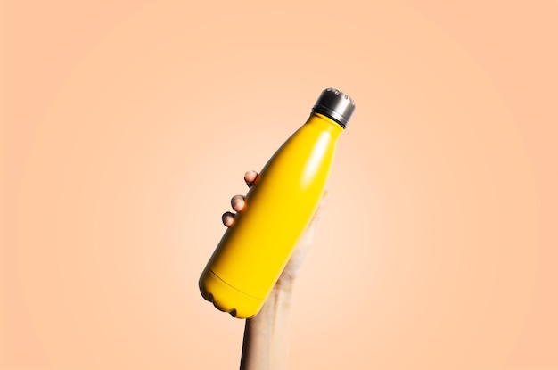 Yellow thermo bottle in hand on background of color of the year peach fuzz