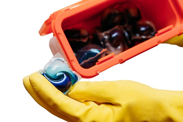 A yellow thick glove holds a gel powder in capsules tablet in the background of a plastic box with