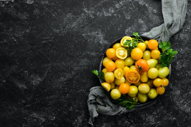 Yellow tomatoes in a black bowl on a black stone background Top view Free space for your text