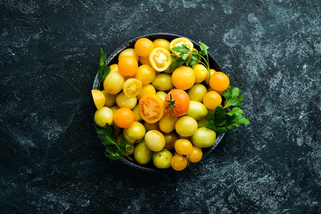 Yellow tomatoes in a black bowl on a black stone background Top view Free space for your text