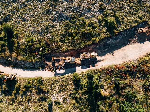 Yellow tracked tractor loads a quarry vehicle with sand view from above