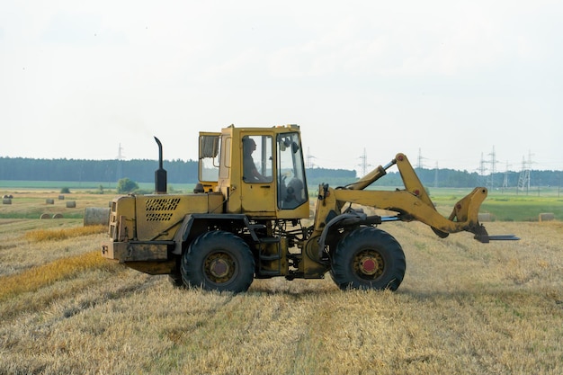 A yellow tractor with the help of a manipulator puts round bales of hay on a trailer Transportation of hay bales in meta storage and drying Preparation of feed for cattle