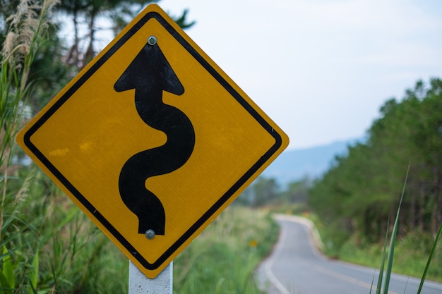 Yellow traffic signs warning against winding road ahead at green grass