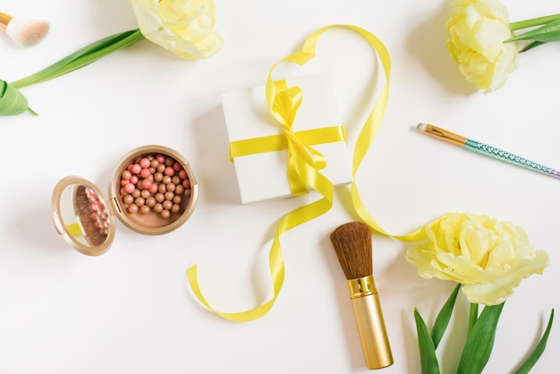 Yellow tulips a gift box with a yellow ribbon and a bow decorative cosmetics on a white background Stylish flat lay fashion blogger