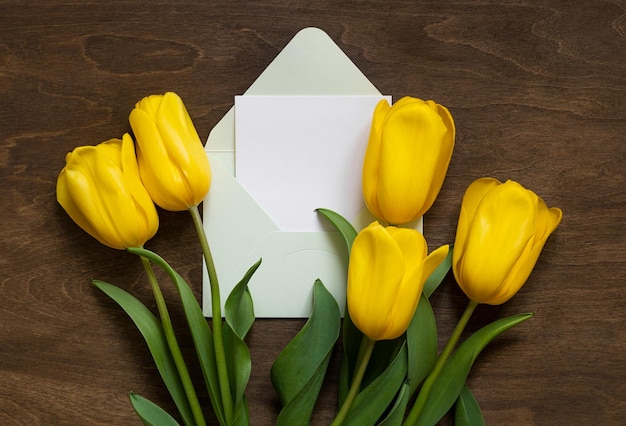 Yellow tulips and green envelope on wooden background