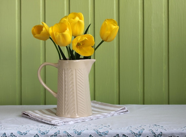 Yellow tulips in a jug on a green board background