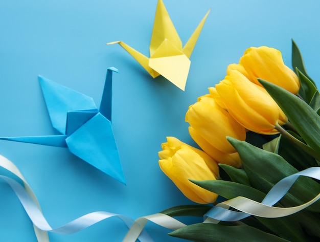 Yellow tulips and origami paper birds on a blue background Colors of the Ukrainian flag Support for Ukraine