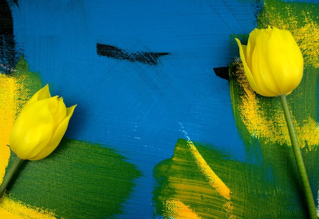 Yellow tulips with eucalyptus leaves flat lay on colourful handmade abstract acrylic background