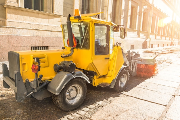 Yellow urban sweeper cleans road embankment dirt with a round brush