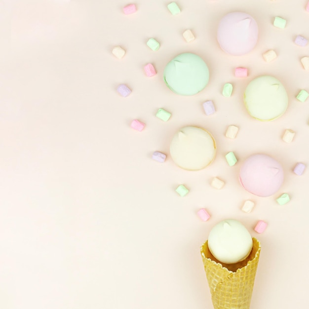 Yellow waffle cone with green, pink and yellow marshmallows looks like macaroons on pastel background.