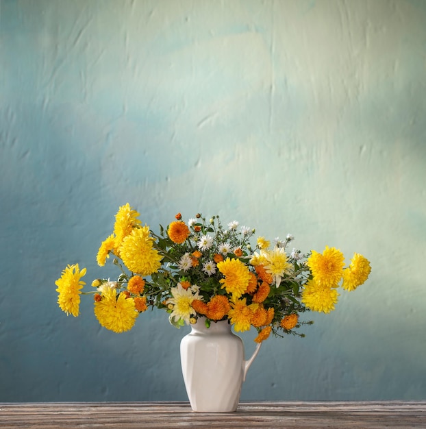 Yellow and white chrysanthemum in white jug on wooden table