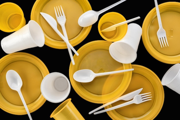 Yellow and white, disposable plastic tableware on a black background. Studio shot, close-up. The con