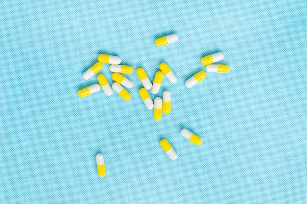 Yellow-white pills on a blue background. Top view of vitamin supplements. Medical concept.