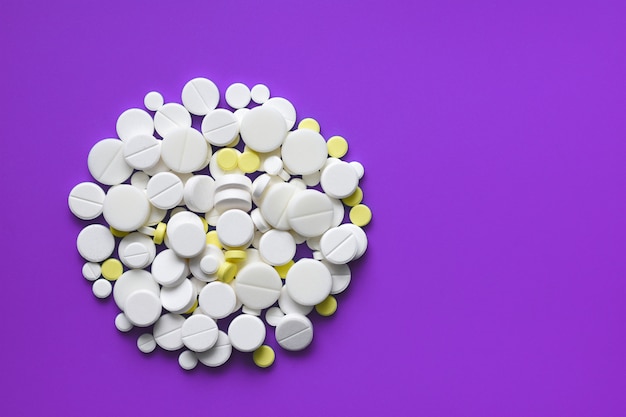 Yellow and white tablets scattered on a violet medical table