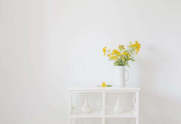 yellow wild summer flowers in jug on white vintage interior