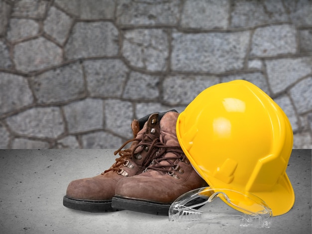 Yellow working hard hat and work boots on wall background