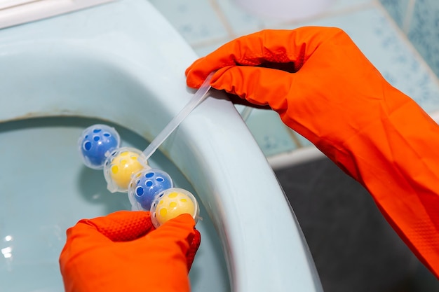 A yellowblue plastic toilet block that cleans the walls of the toilet and refreshes the bathroom A girl in latex red gloves hangs a toilet block