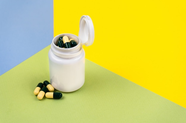 Yellowgreen pills in a white jar on colored Food supplement multivitamins herbal medicines