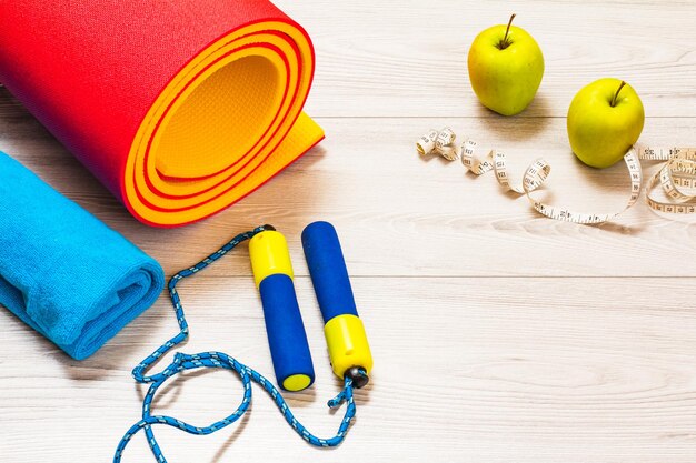 Yoga mat and different tools for fitness on floor in room.