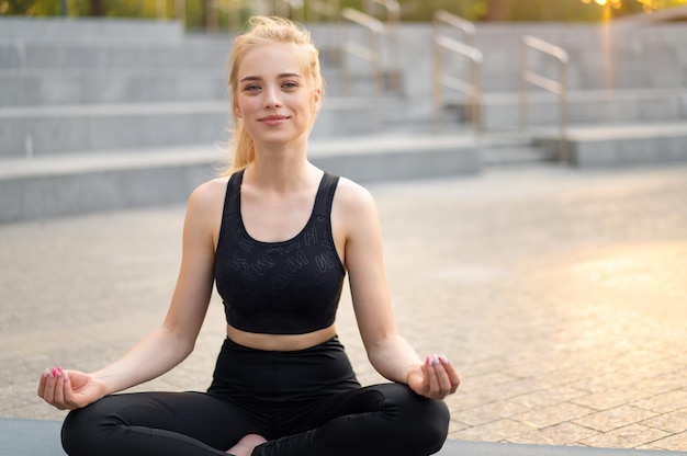 Yoga and Meditation in Modern City Caucasian Woman Relax Lotus Position Sitting Yoga Mat Outdoors Summer Park on Concrete floor Young Adult Fit Female Relaxing after Yoga Practice Workout Siddhasana