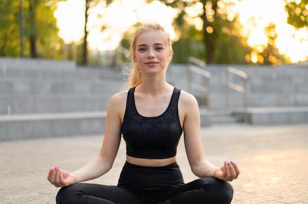 Yoga and Meditation in Modern City Caucasian Woman Relax Lotus Position Sitting Yoga Mat Outdoors Summer Park on Concrete floor Young Adult Fit Female Relaxing after Yoga Practice Workout Siddhasana