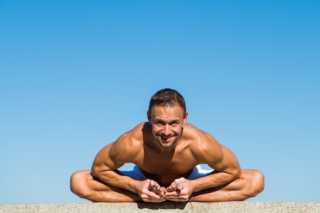 Yoga practice helps find harmony and balance Man practicing yoga blue sky background Reached