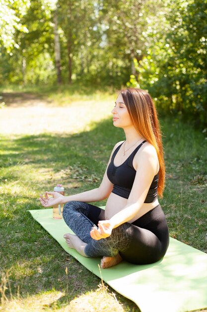 Yoga for pregnant women A beautiful pregnant woman goes in for sports trains in nature in the park meditation harmony sunlight Vertical