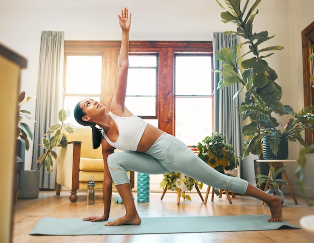 Yoga stretching and fitness woman in health training and workout at home or living room for wellness and balance Young biracial sports person in pilates or side plank for holistic body exercise