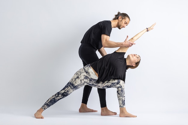 Yoga teacher correcting posture to his student isolated on white background