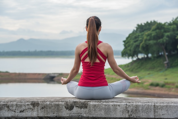 Yoga woman doing meditation at the lake, back view.