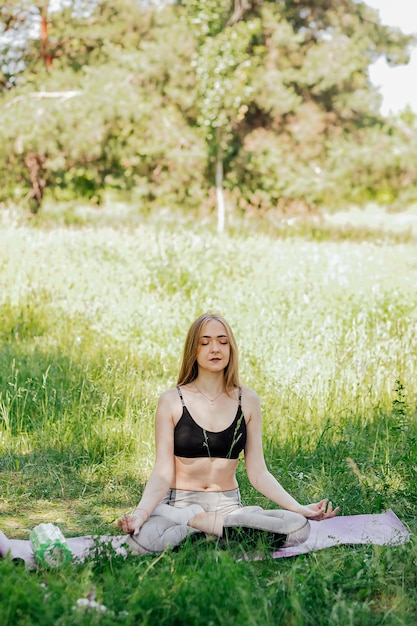 Yoga woman on green grass girl relaxes in the field Yoga woman in green park girl doing gymnastics outdoors Meditating woman in meditation in yoga pose practices outdoors