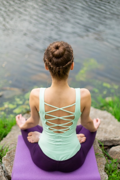 Yoga woman practicing yoga lesson, breathing, meditation, doing exercise Ardha Padmasana, half lotus pose with mudra gesture, closeup in summer on nature against the  of water