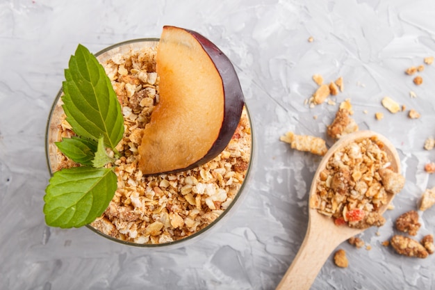 Yoghurt with plum, chia seeds and granola in a glass and wooden spoon. top view