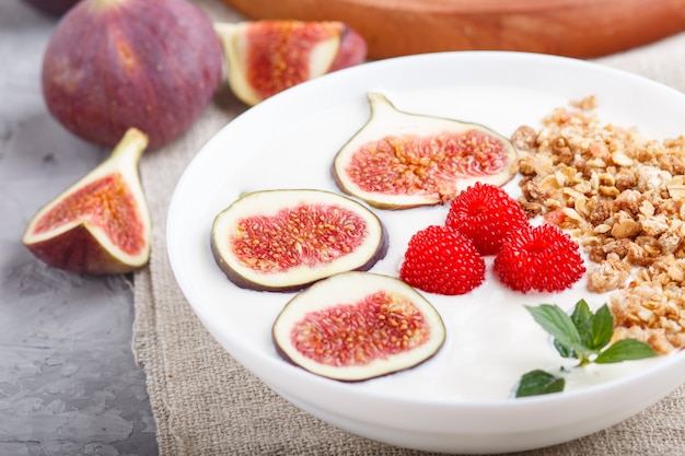 Yoghurt with raspberry, granola and figs in white plate on a gray concrete background 