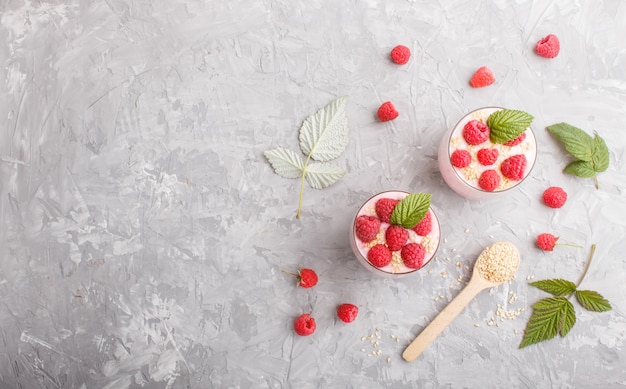 Yoghurt with raspberry and sesame in a glass and wooden spoon on gray concrete background. top view.