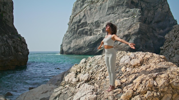 Yogi girl stretching body on rocky seacoast African american woman making yoga