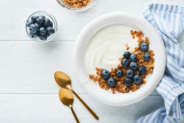 Yogurt Greek Yogurt with granola and fresh blueberries in white bowl over old white wood background Morning breakfast concept Healthy food for breakfast top view