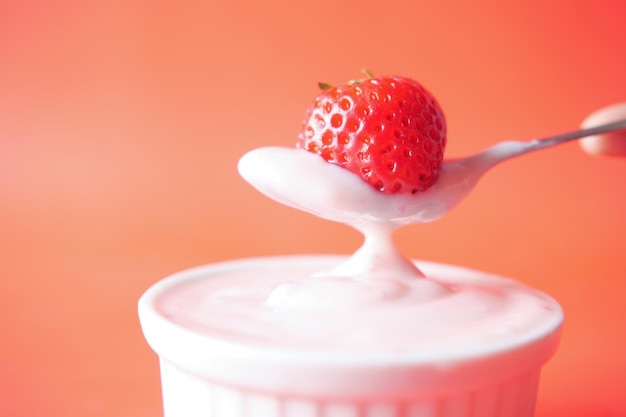 Yogurt and strawberry on a spoon on red background