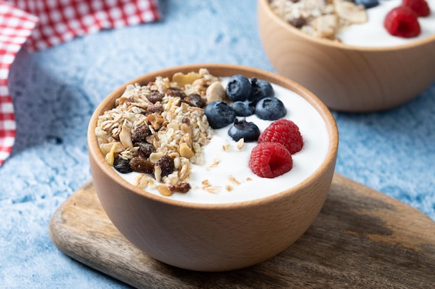 Yogurt with berries and muesli for breakfast in bowl on blue background