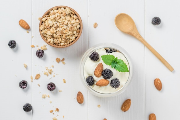 Yogurt with granola blackberries and almonds on a white wooden table